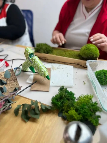 Účastnice kurzu aranžují stabilizovaný mech do dřevěné misky pomocí tavné pistole a přírodních materiálů